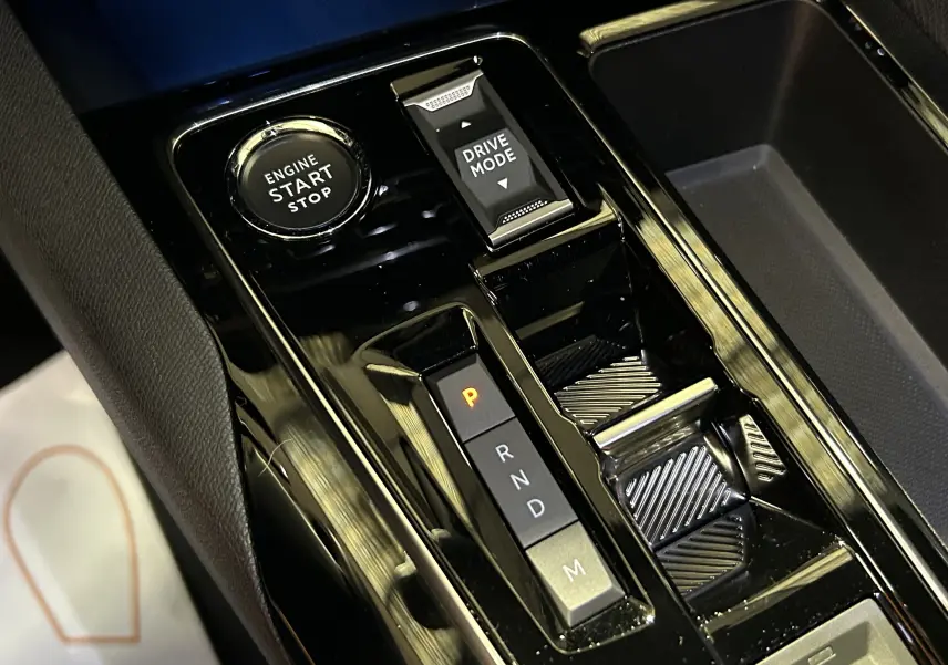 Gros plan sur la console centrale noire brillante du Peugeot 5008 2024 avec bouton start/stop et sélecteur de mode de conduite.