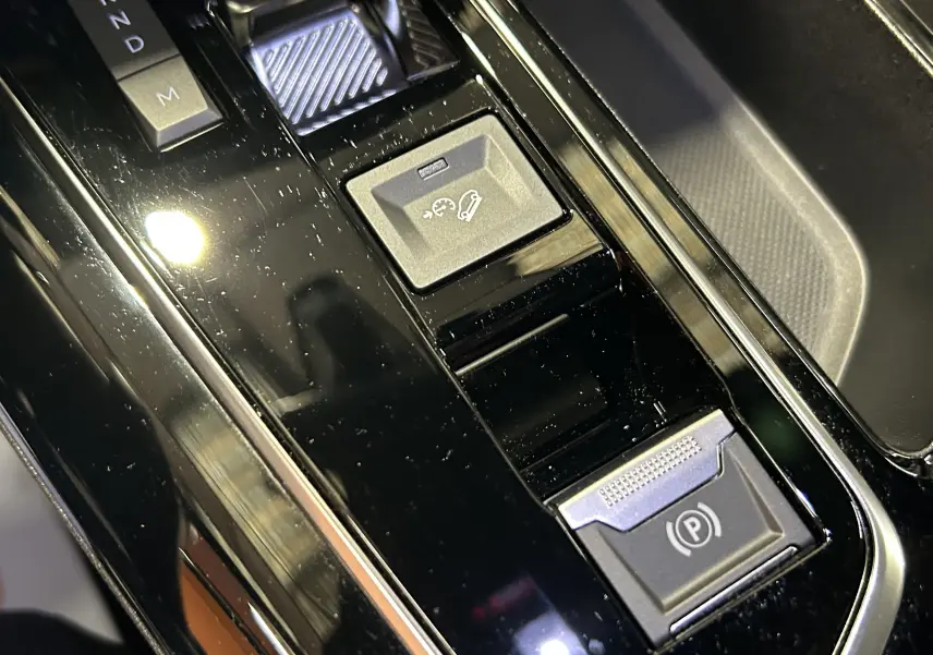 Gros plan sur la console centrale noire brillante du Peugeot 5008 2024 avec commandes de boîte auto et frein électrique.