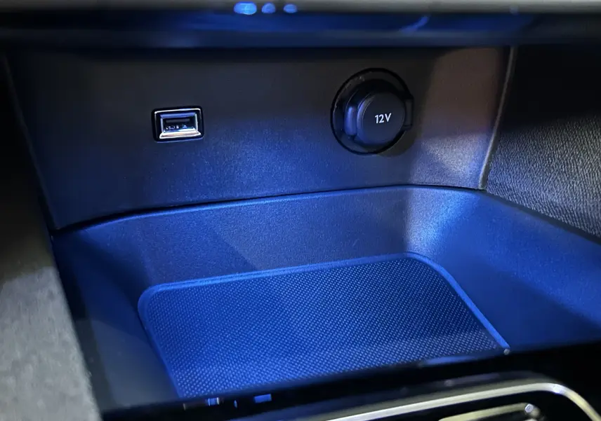 Prise 12V et port USB éclairés en bleu dans le compartiment de rangement central du Peugeot 5008 Gris Platinium 2024.