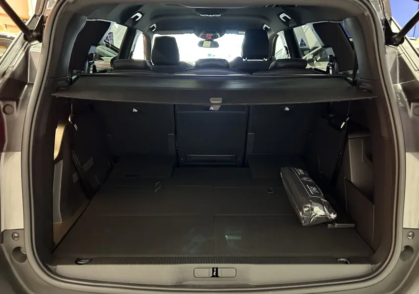 Coffre ouvert vu de l'arrière d'un Peugeot 5008 Gris Platinium 2024 avec banquette rabattue et cache-bagages noir.
