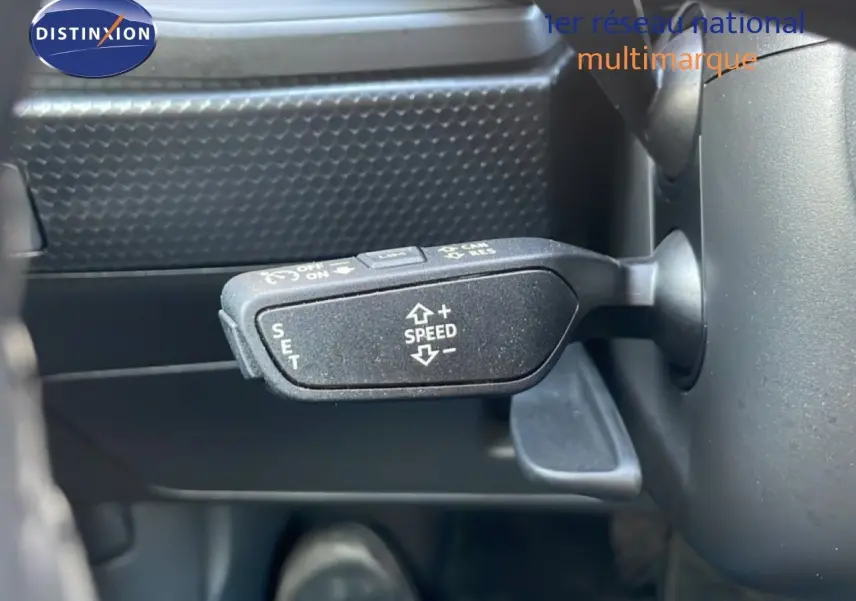 Gros plan sur la commande de régulateur de vitesse à gauche du volant dans l'Audi A1 Sportback blanc glacier 2023.