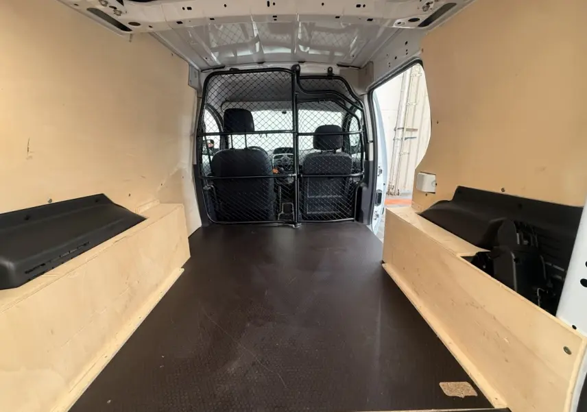 Vue intérieure arrière du Renault Kangoo blanc 2016, montrant l'espace de chargement avec cloison tubulaire noire.