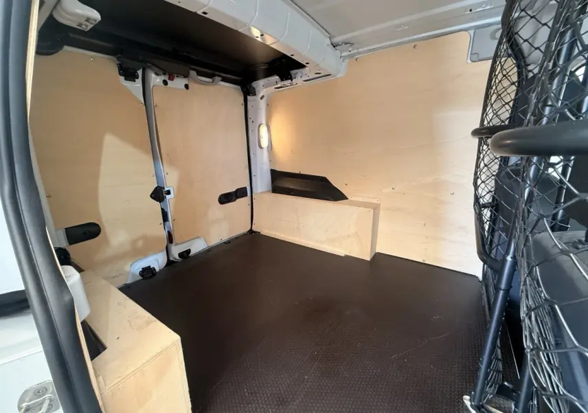 Intérieur du coffre du Renault Kangoo blanc vu de l'arrière, avec cloison tubulaire et revêtement bois clair.