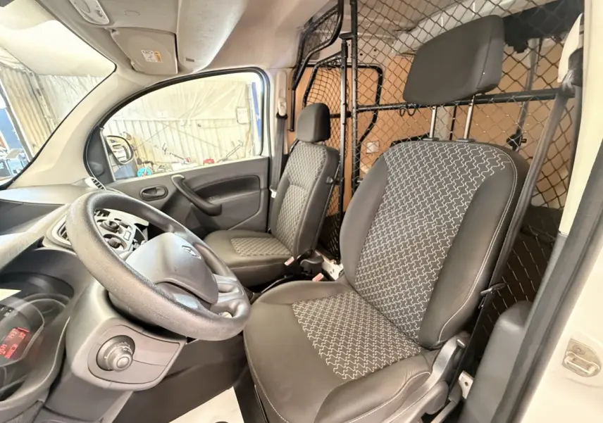 Vue intérieure côté conducteur du Renault Kangoo blanc 2016 avec cloison tubulaire pleine et sièges tissu noir à motifs.