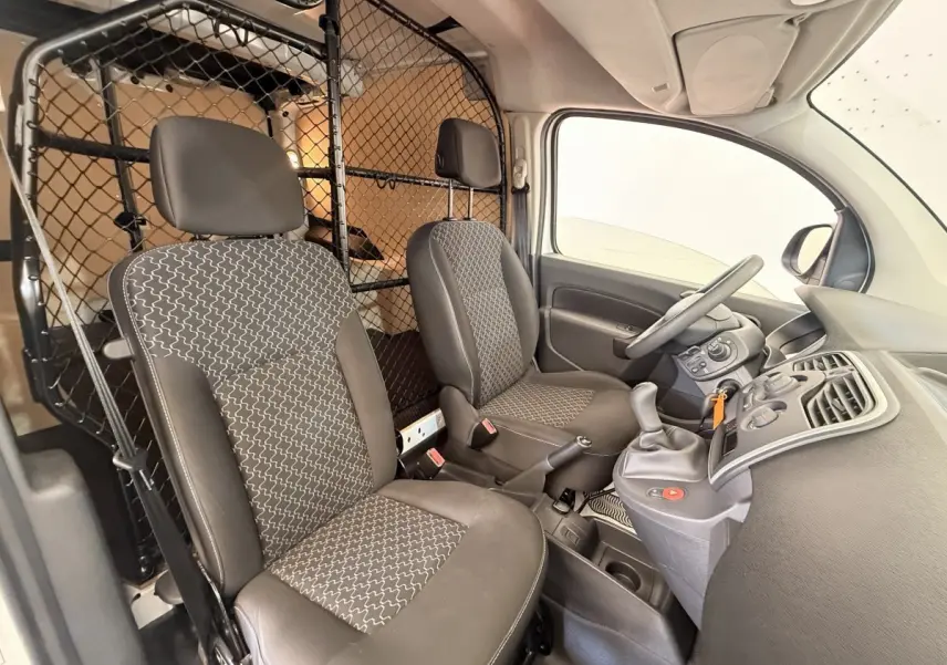 Vue intérieure côté conducteur du Renault Kangoo blanc 2016 avec cloison tubulaire et sièges gris à motifs.