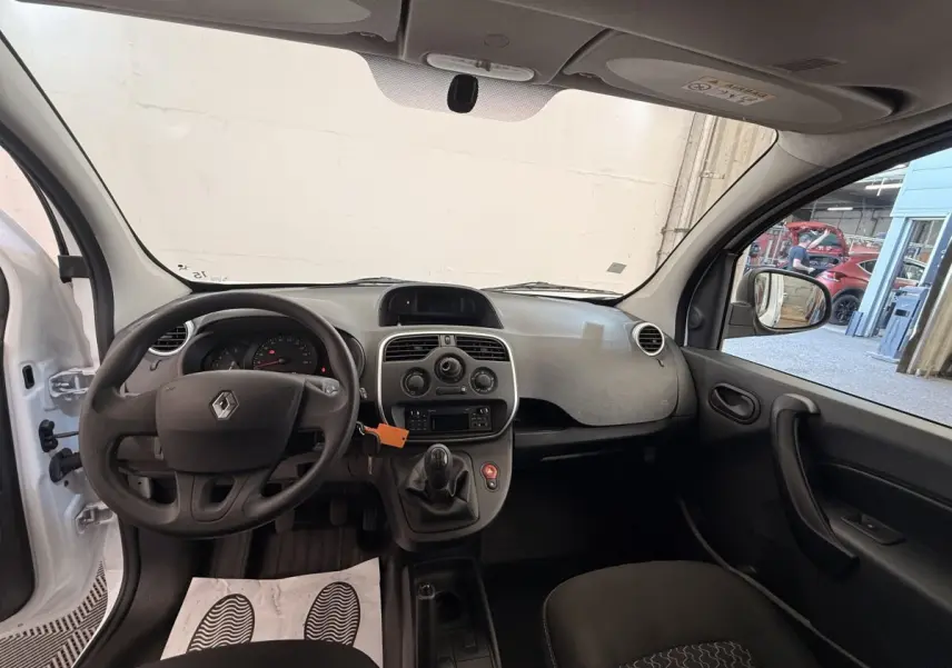 Intérieur avant du Renault Kangoo blanc 2016, vue côté conducteur avec volant, tableau de bord et levier de vitesses manuelle visibles.