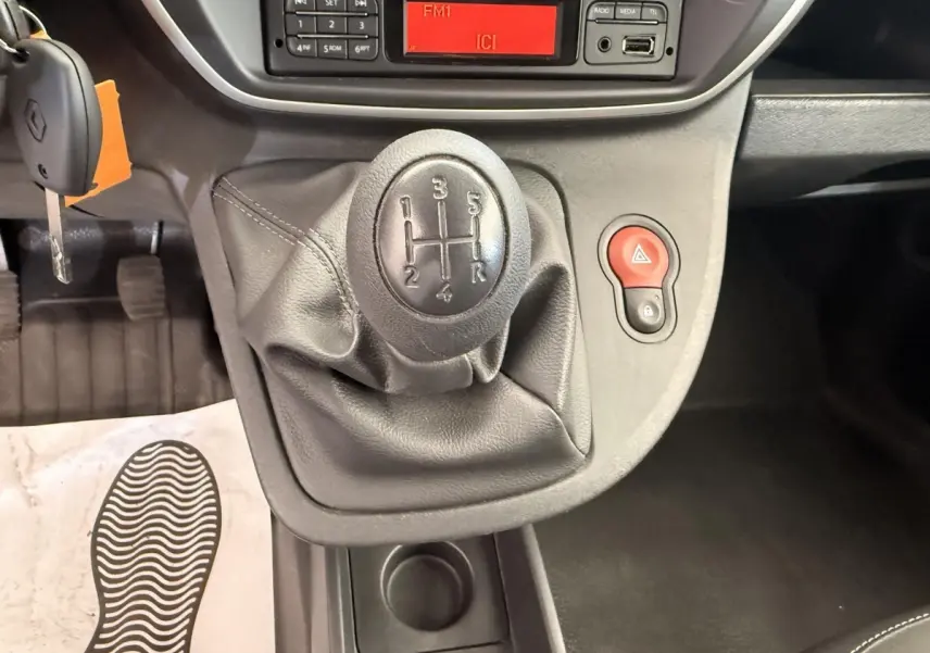 Gros plan sur le levier de vitesses manuel noir du Renault Kangoo Confort Energy dCi 75, avec tableau de bord et bouton de warning rouge visible.