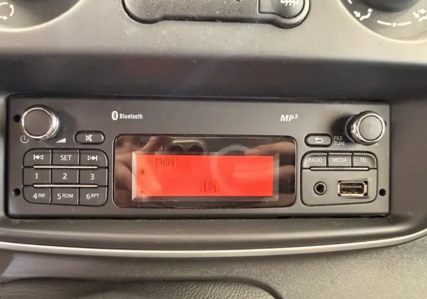 Gros plan sur la radio MP3 avec écran rouge et commandes Bluetooth du tableau de bord du Renault Kangoo blanc.