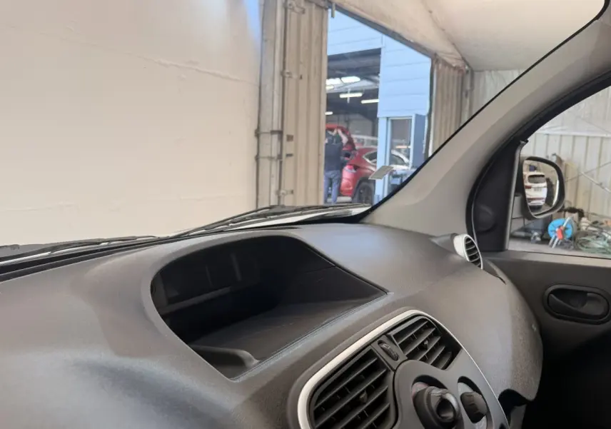 Vue intérieure côté passager du tableau de bord noir du Renault Kangoo blanc, avec prise d'air et porte.