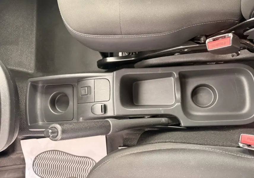 Vue plongeante sur la console centrale noire entre les sièges avant du Renault Kangoo blanc, frein à main et rangements visibles.