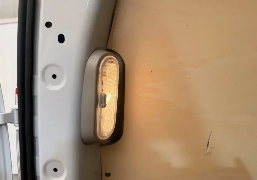 Gros plan sur l’éclairage intérieur blanc allumé dans la zone de chargement d’un Renault Kangoo blanc, cloison bois visible.