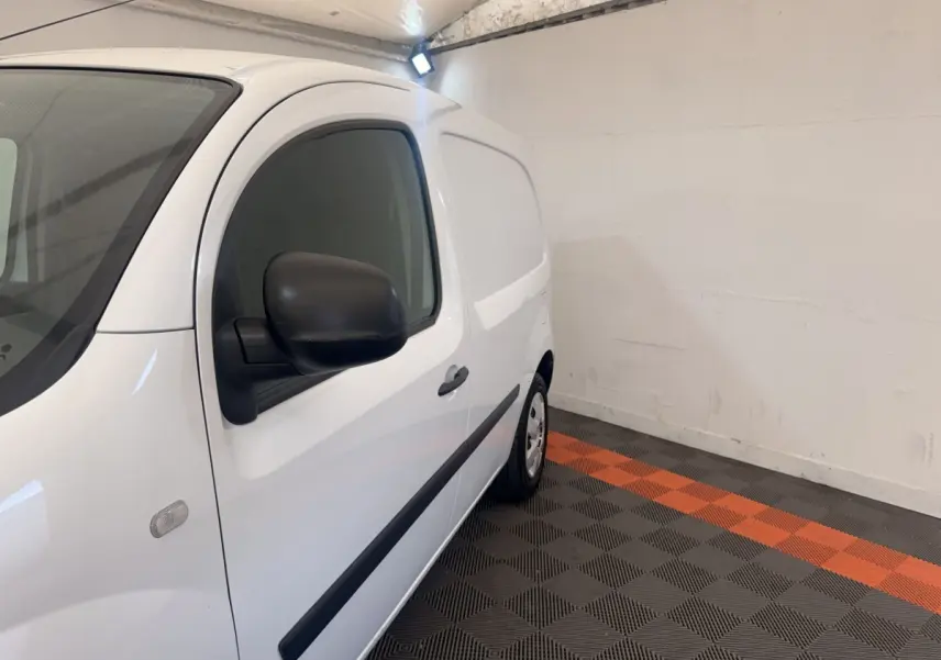 Vue de profil côté gauche d’un Renault Kangoo blanc 2016 en intérieur avec rétroviseurs noirs et bande latérale noire.