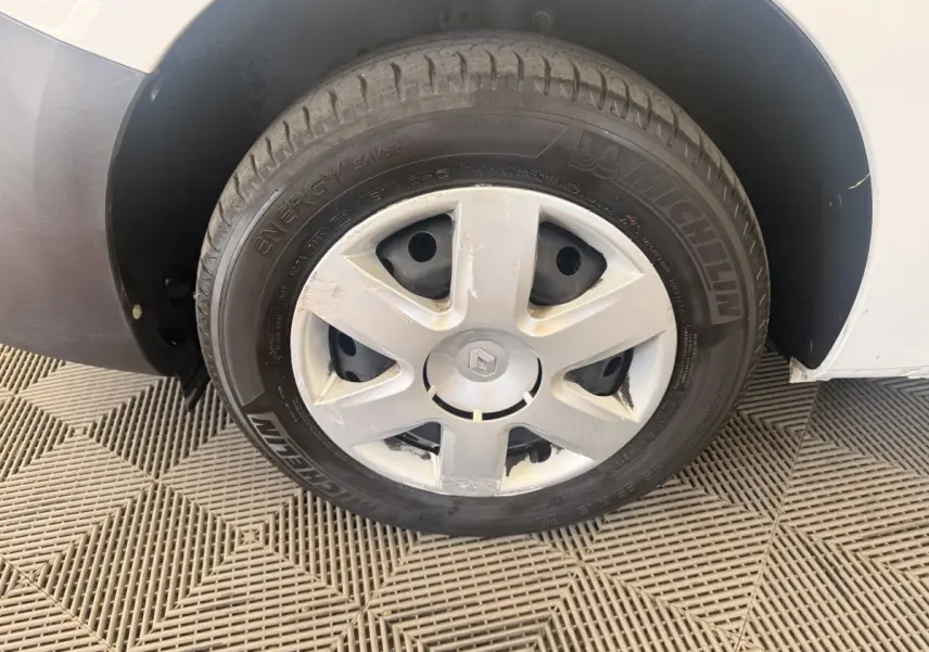 Gros plan sur la roue avant gauche d’un Renault Kangoo blanc avec jante acier et enjoliveur abîmé.