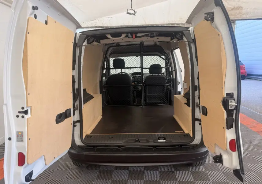 Vue arrière du Renault Kangoo blanc 2016 avec portes ouvertes montrant l'espace de chargement protégé par une cloison tubulaire.