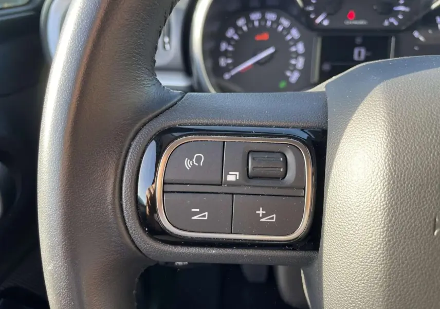 Gros plan sur les commandes audio au volant d'une Citroën C3 1.2 Shine 2021, volant en cuir noir.