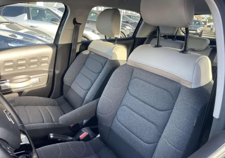 Intérieur de la Citroën C3 2021, vue côté conducteur, sièges bi-ton gris foncé et clair avec accoudoir central.