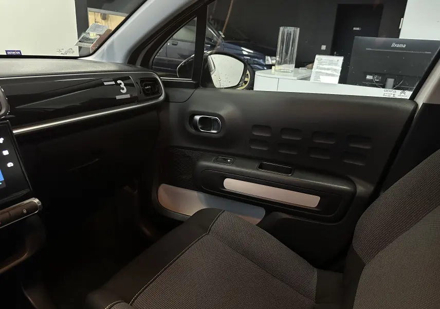 Vue intérieure côté passager de la Citroën C3 blanche, montrant la porte et le siège gris foncé avec détails texturés.
