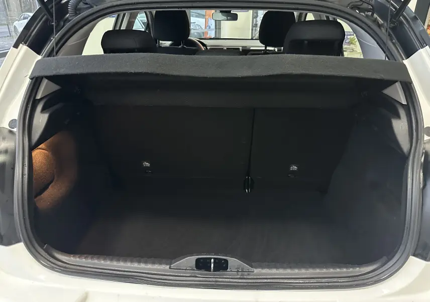 Coffre ouvert vu de l'arrière d'une Citroën C3 blanche, intérieur noir avec cache-bagages relevé.