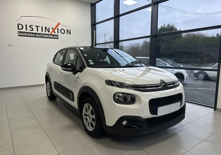 Citroën C3 blanc vue 3/4 avant droit en intérieur, avec protections latérales noires et toit noir contrasté.