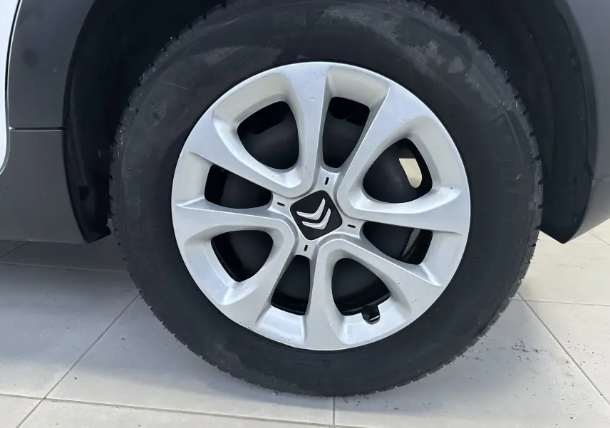 Gros plan sur la roue avant droite d'une Citroën C3 blanche, mettant en valeur la jante en alliage argentée au design distinctif.