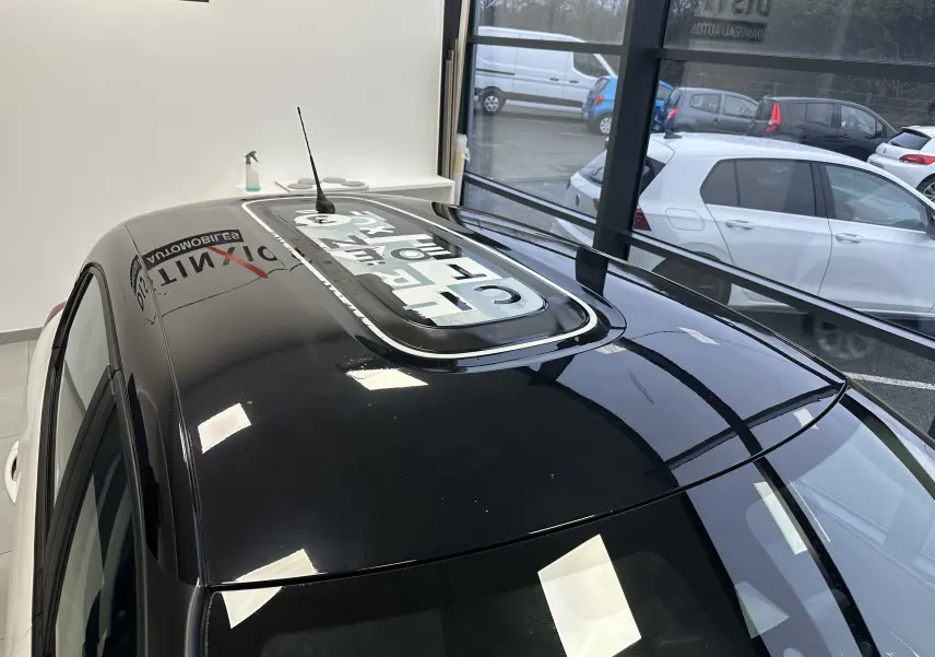 Toit noir brillant avec toit ouvrant panoramique sur une Citroën C3 blanche vue en 3/4 arrière intérieur showroom.