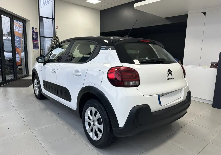 Vue 3/4 arrière droite d'une Citroën C3 blanche avec toit noir et protections latérales noires en concession.