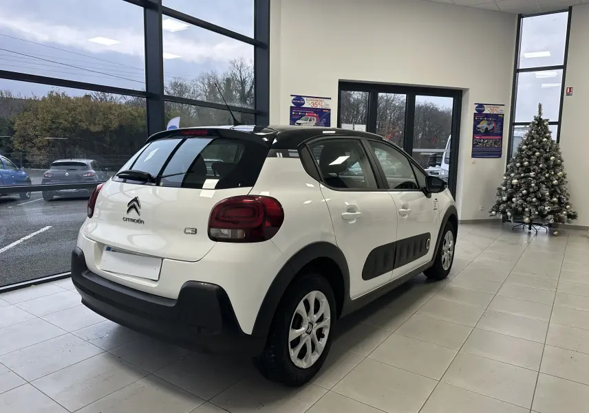 Citroën C3 blanc vue 3/4 arrière droit en intérieur, avec toit noir et protections latérales noires.