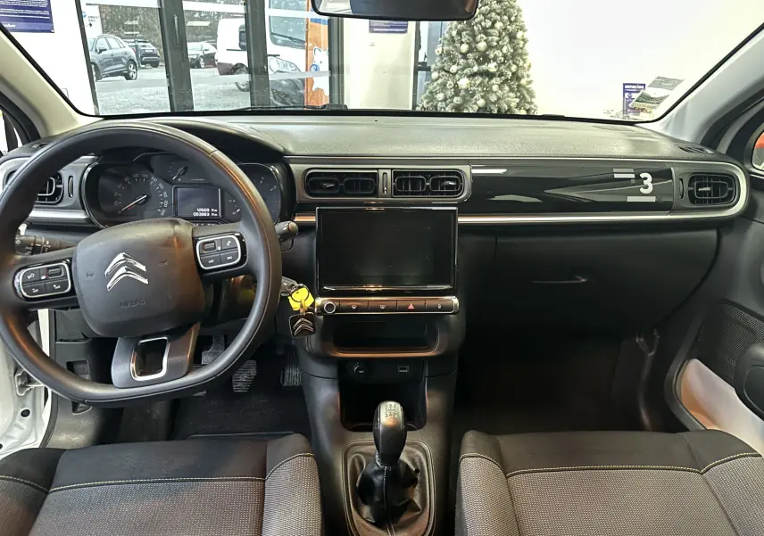 Vue intérieure avant de la Citroën C3 blanche de 2018, tableau de bord noir avec écran tactile et levier de vitesse manuel.