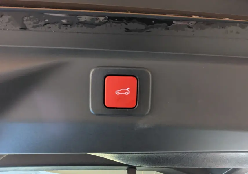 Bouton rouge de fermeture électrique du hayon visible à l'intérieur du coffre du Peugeot 3008 blanc Okenite.