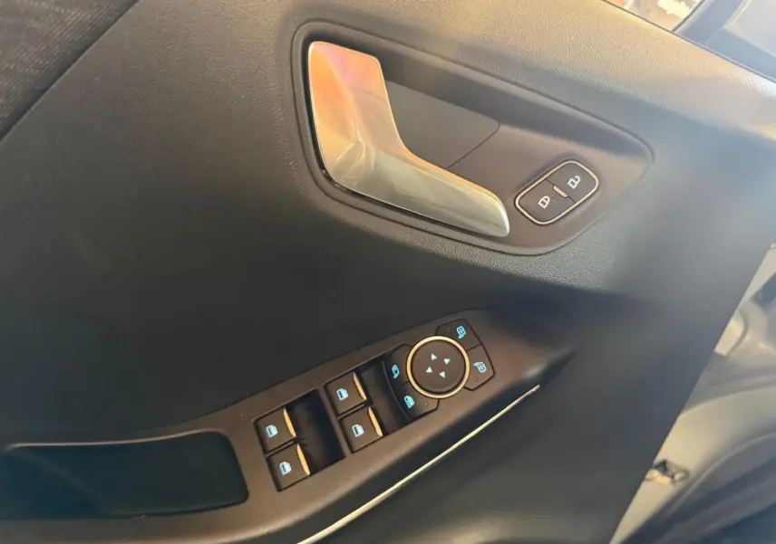 Gros plan sur la porte avant gauche du Ford Puma gris, montrant la poignée chromée et les commandes électriques des vitres.