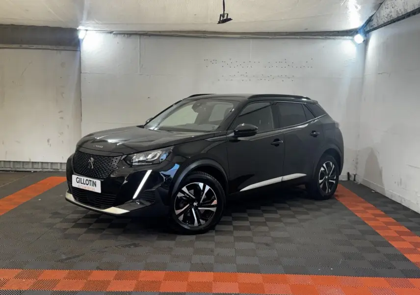 Peugeot 2008 noir en 3/4 avant droit, avec jantes alliage bicolores et feux LED distinctifs, stationné en intérieur.