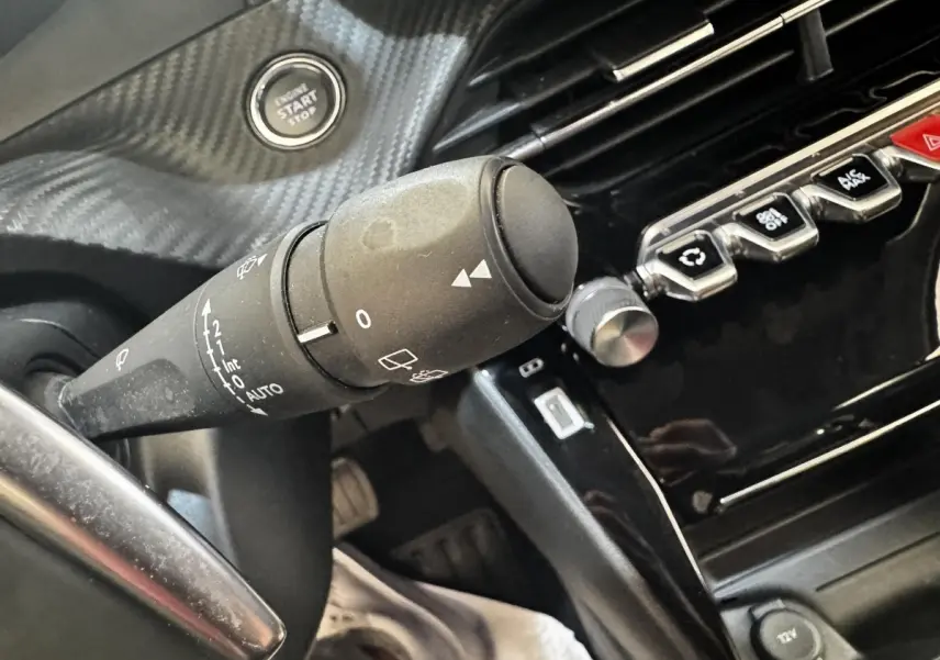 Gros plan sur la commande d’essuie-glace et le bouton démarrage d’un Peugeot 2008 noir, intérieur moderne avec finition carbone.