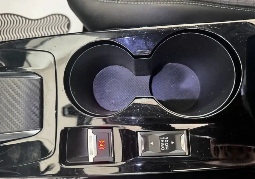 Gros plan sur la console centrale noire du Peugeot 2008, avec porte-gobelets et boutons frein électrique et mode de conduite.