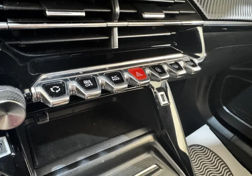 Gros plan sur la console centrale noire du Peugeot 2008 2022, avec rangements et rangée de boutons chromés dont le bouton d'alerte rouge.