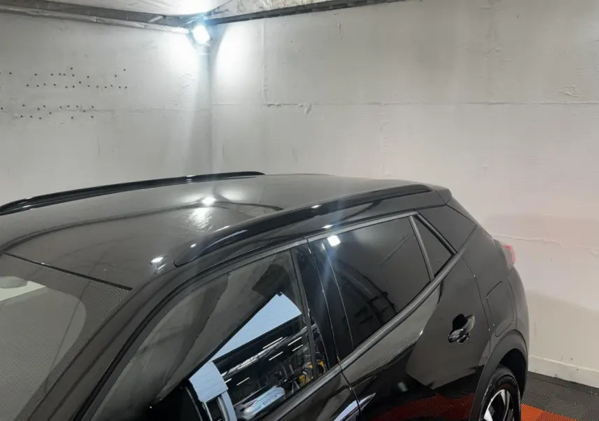 Vue latérale droite d’un Peugeot 2008 noir brillant avec vitres teintées et barres de toit dans un garage.