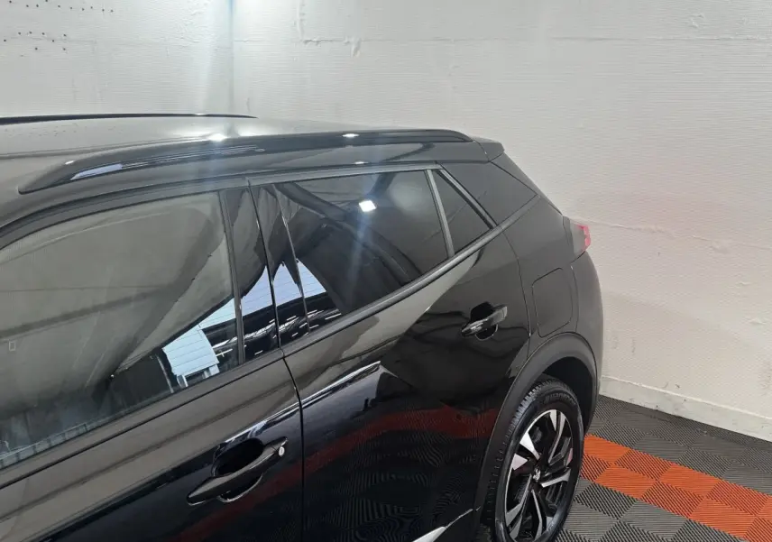 Vue côté droit arrière du Peugeot 2008 noir avec jantes alliage et barres de toit assorties.