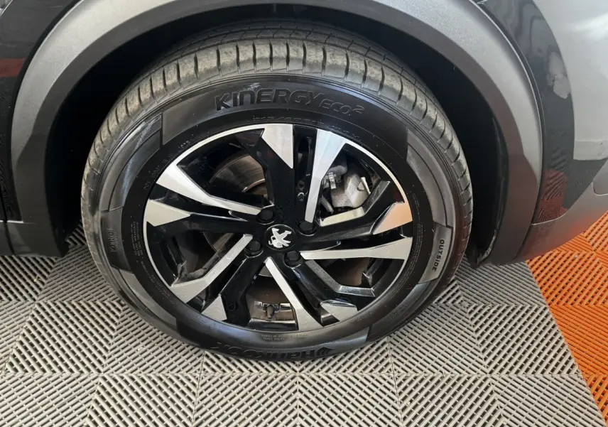 Gros plan sur la roue avant droite noire du Peugeot 2008 2022 avec jante alliage bicolore et logo lion central.