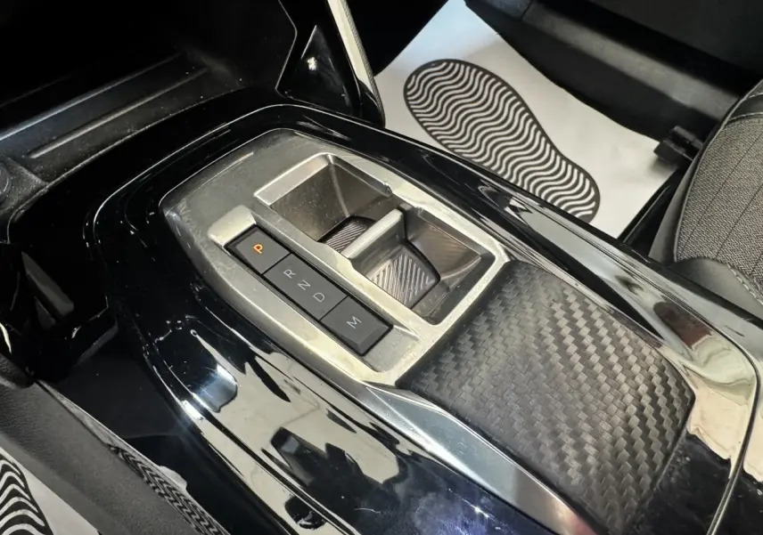 Gros plan sur la console centrale noire brillante du Peugeot 2008 avec sélecteur de boîte automatique et finition carbone.