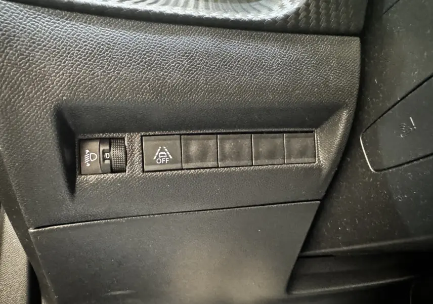 Détail intérieur montrant les commandes de réglage des phares et de désactivation de l'assistance au maintien de voie sur Peugeot 2008 noir.