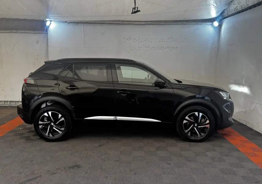 Profil côté gauche d’un Peugeot 2008 noir 2022 avec jantes alliage bicolores et barres de toit assorties.