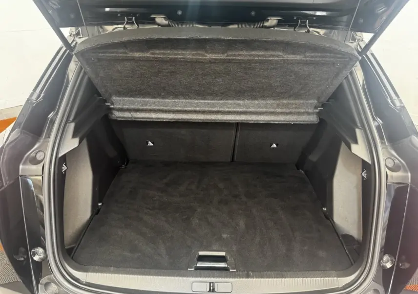 Coffre ouvert vu de l'arrière d'un Peugeot 2008 noir, montrant l'espace de chargement et la tablette cache-bagages relevée.