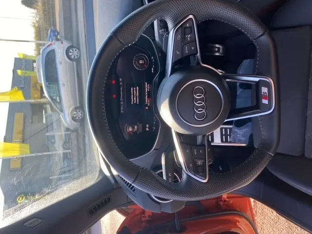 Vue intérieure centrée sur le volant perforé Audi TT orange 2021 avec commandes multifonctions et affichage numérique.