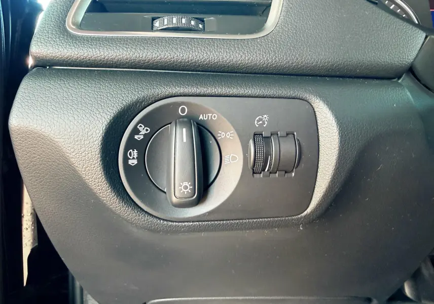 Gros plan sur le bouton de commande des phares noir dans l'habitacle d'un Audi Q3 noir, côté gauche du tableau de bord.