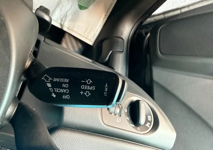 Gros plan sur la commande de régulateur de vitesse à gauche du volant dans l’habitacle noir d’un Audi Q3 noir.