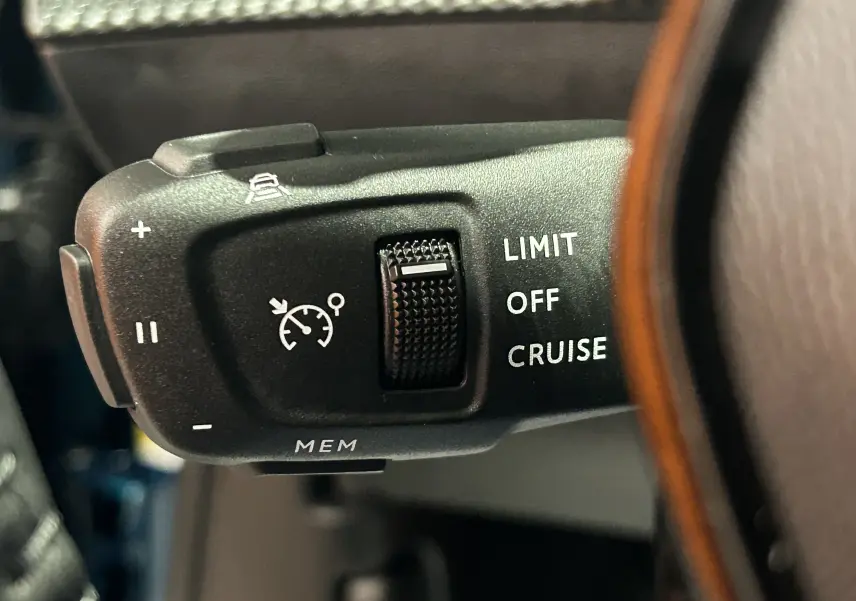 Gros plan sur la commande de régulateur de vitesse au volant du Peugeot 2008 bleu Obsession, intérieur sombre.