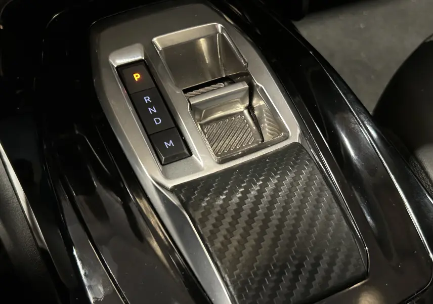 Gros plan sur la console centrale noire avec sélecteur de boîte auto et finition carbone du Peugeot 2008 Bleu Obsession.