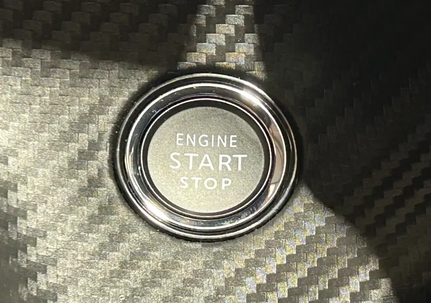 Gros plan sur le bouton Engine Start Stop entouré d’un cerclage chromé sur fond de finition carbone intérieure.