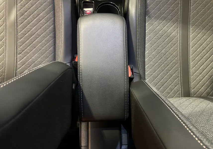 Vue plongeante sur l'accoudoir central en cuir noir et les sièges tissu gris du Peugeot 2008 II Ph.2 Allure Hybrid 2025.