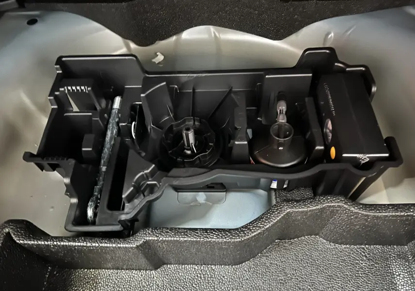 Vue rapprochée de l’espace de rangement sous coffre du Peugeot 2008 bleu, montrant les outils et accessoires intégrés.