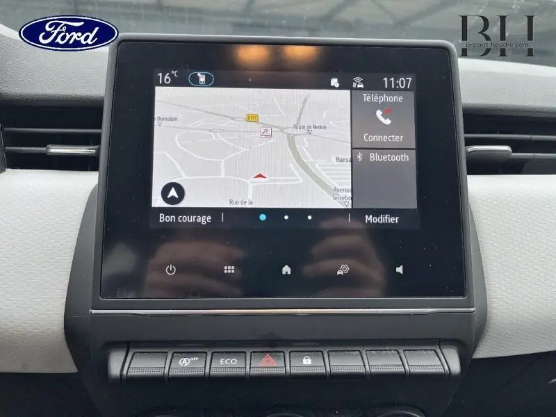 Écran tactile central avec navigation et commandes sur tableau de bord gris clair de Renault Clio blanc, vue intérieure frontale.